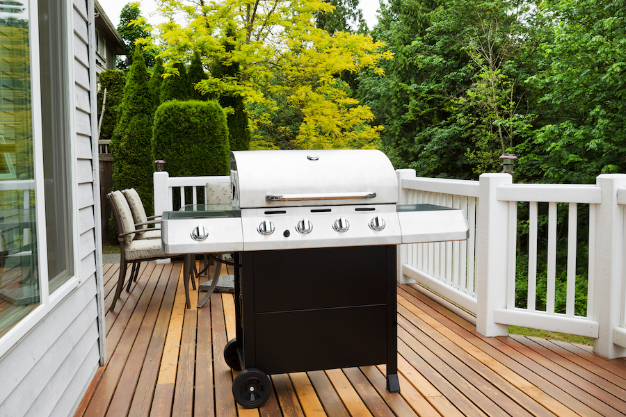 Closeup horizontal photo of BBQ grill on open cedar patio with seasonal trees in full bloom in background