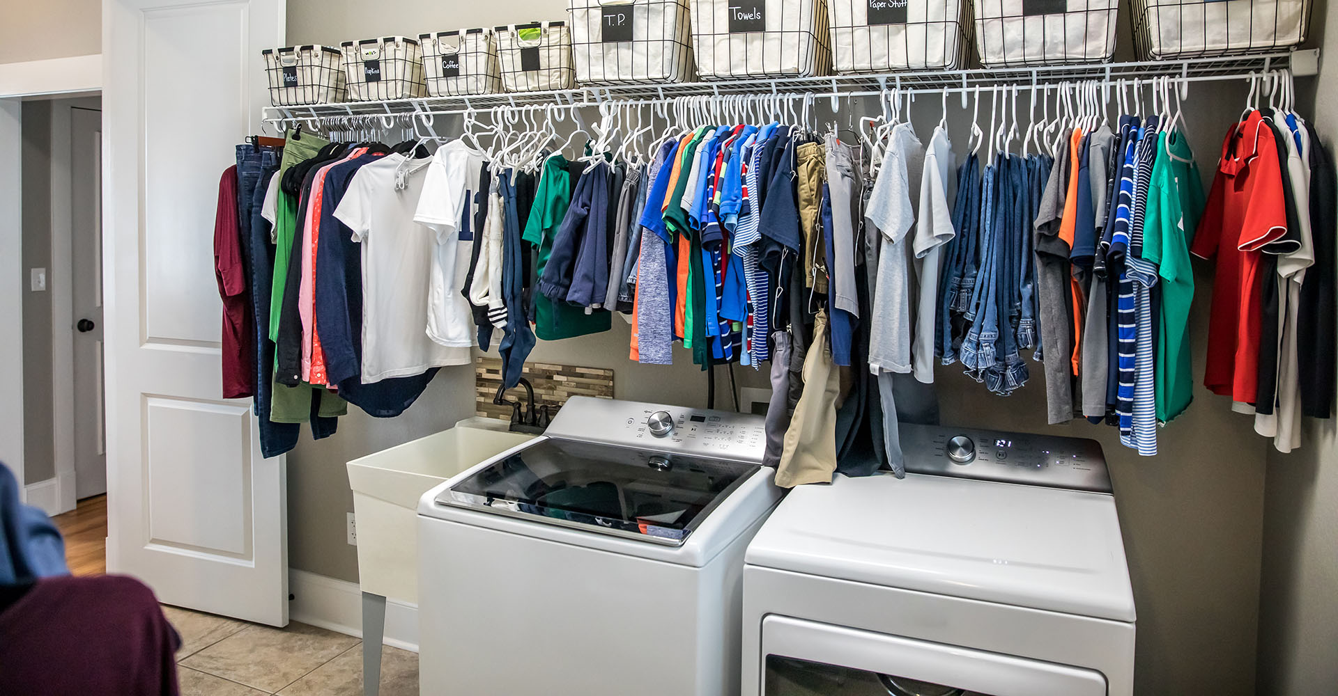 An organized laundry room with many clean shirts being hung to d