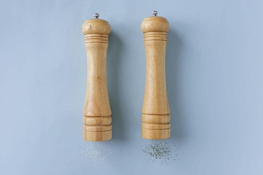 Set of wooden pepper and salt grinders or mills lying on their sides on a blue background with lateral copy space